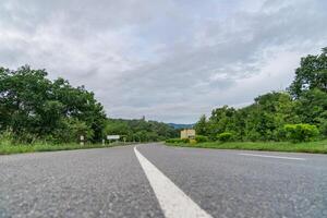 A ground-level perspective of a rural street in Tak Province, Thailand, in open sky during the day. This road serves as key transportation artery to western region of country. photo