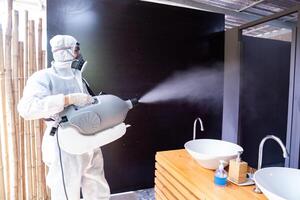 Professional technical man in prevention suit with his sterilizing machine and disinfecting water sprays in toilet or wc area field for purifying coronavirus COVID-19 photo