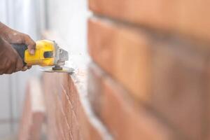 Close up to Grinder Machine in Worker man hand hold saw, grind, check and kept detailed polyurethane foam Brick wall with dust all around. photo