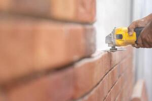 Close up to Grinder Machine in Worker man hand hold saw, grind, check and kept detailed polyurethane foam Brick wall with dust all around. photo