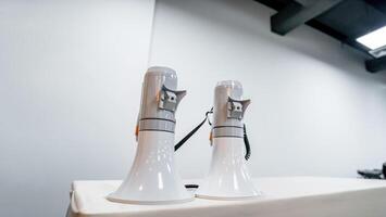 Two white - gray MEGAPHONE are laid on cream table in empty hall, ready to used for event corona virus vaccine booster in Bangkok, Thailand. photo