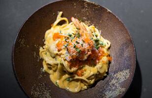 Spaghetti Carbonara pasta Egg and Cheese creamy cream sauce with Shrimp and micro herb decoration on the top of it of earthware circle bowl in studio light. photo