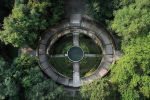 Aerial view of a circular stone structure with a central pond, surrounded by lush green trees. photo