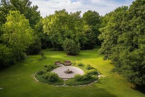 Serene garden with circular stone patio, benches, and lush greenery. photo