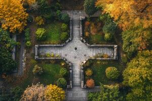 Aerial view of a stone cross-shaped garden path surrounded by autumn foliage. photo
