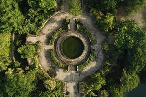 Aerial view of a circular pond surrounded by lush greenery and stone pathways. photo