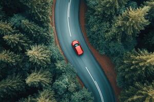 Aerial view of red car driving on winding road through lush green forest. photo