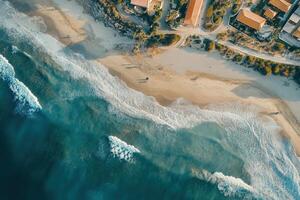 Aerial view of ocean waves crashing on sandy beach near coastal buildings. photo
