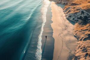 Aerial view of person walking on secluded beach at sunset. photo