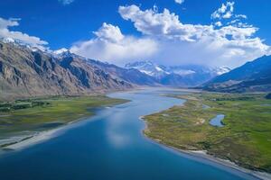 Aerial view of a serene river flowing through a valley, surrounded by mountains and lush greenery under a vibrant blue sky. photo
