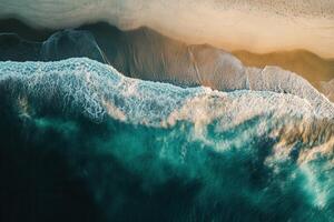 Aerial view of ocean waves crashing on sandy beach at sunset. photo