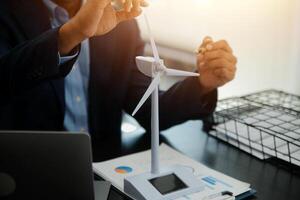 Shut of handsome business man working on new alternative energy development looking at a model of a wind turbine in modern startup. photo
