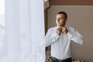 A man in a white shirt is getting dressed in front of a window photo