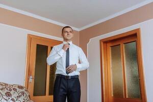 A man in a suit is standing in front of a door, getting ready to tie his tie photo