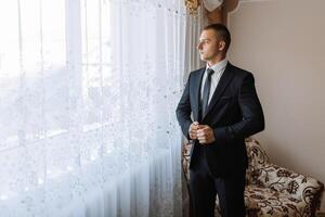 A man in a suit is standing in front of a window, looking out at the street photo