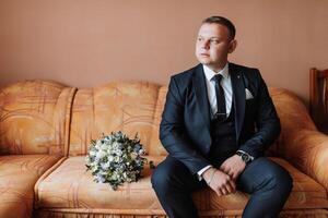 A man in a suit sits on a couch with a bouquet of flowers in front of him photo