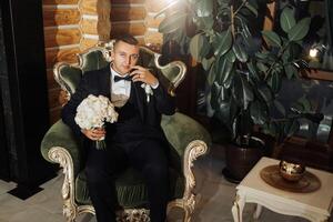 A man in a suit is sitting in a green chair with a bouquet of flowers in his lap photo