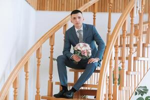A man in a suit is sitting on a staircase holding a bouquet of flowers photo