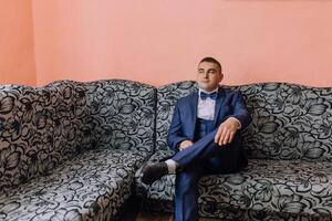 A man in a suit and bow tie sits on a couch photo