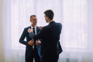 Two men in suits are standing in front of a window photo