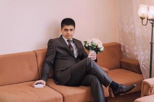 A man in a suit is sitting on a couch holding a bouquet of flowers photo