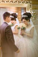 A bride and groom are standing in front of a mirror, the bride holding a bouquet photo