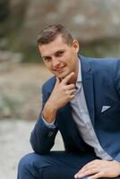 A man in a blue suit is sitting on the ground and looking at the camera photo