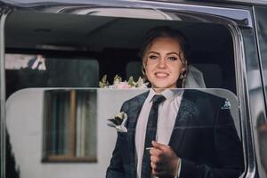 A man in a suit and tie is smiling as he stands in a car window photo