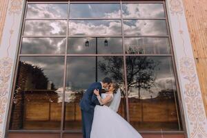 A bride and groom are kissing in front of a large window photo