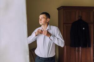 A man in a white shirt is getting dressed in front of a window photo