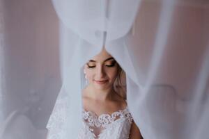 A bride is standing in front of a curtain, with her face partially hidden photo