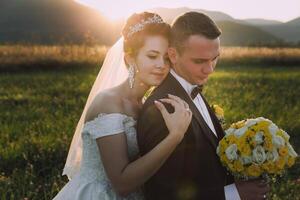 A bride and groom are embracing in a field with a bouquet of yellow flowers photo