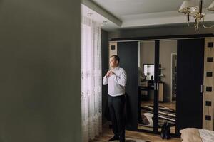 A man is getting dressed in a room with a window and a mirror photo