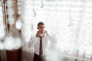 A man is getting ready for a wedding, putting on a tie and adjusting his collar photo