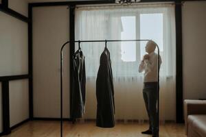 A man is standing in front of a clothes rack with a dress hanging from it photo