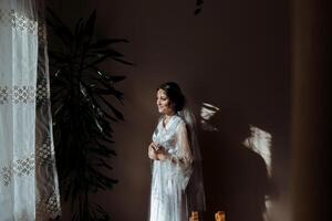 A woman in a white gown stands in front of a window with a potted plant behind h photo