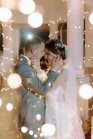 A bride and groom are embracing in front of a lighted backdrop photo