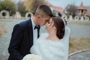 A bride and groom are kissing each other's cheeks in front of a building photo