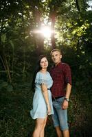 A man and a woman are standing in a forest, smiling at the camera photo