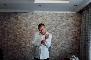 A man is getting dressed in front of a wall with a patterned wallpaper photo