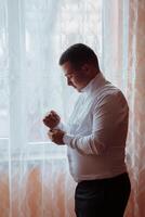 A man in a white shirt is getting dressed in front of a window photo