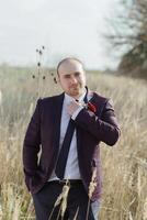 A man in a purple suit and tie stands in a field of tall grass photo