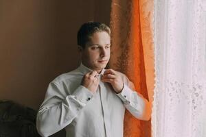 A man in a white shirt is getting dressed in front of a window photo