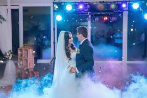 A bride and groom are dancing in a room with a fog machine photo