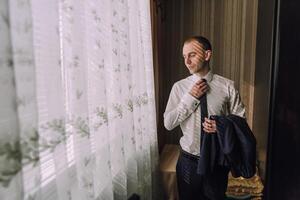 A man is getting ready for a formal event, putting on a tie and jacket photo
