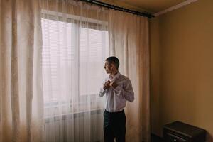 A man is getting dressed in front of a window photo