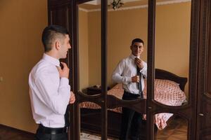 A man is getting ready to tie his tie in front of a mirror photo