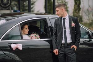 A man and a woman are standing in front of a black car photo