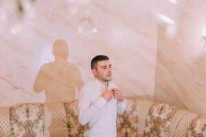 A man is getting dressed in front of a couch photo