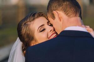A bride and groom are hugging each other, both smiling photo